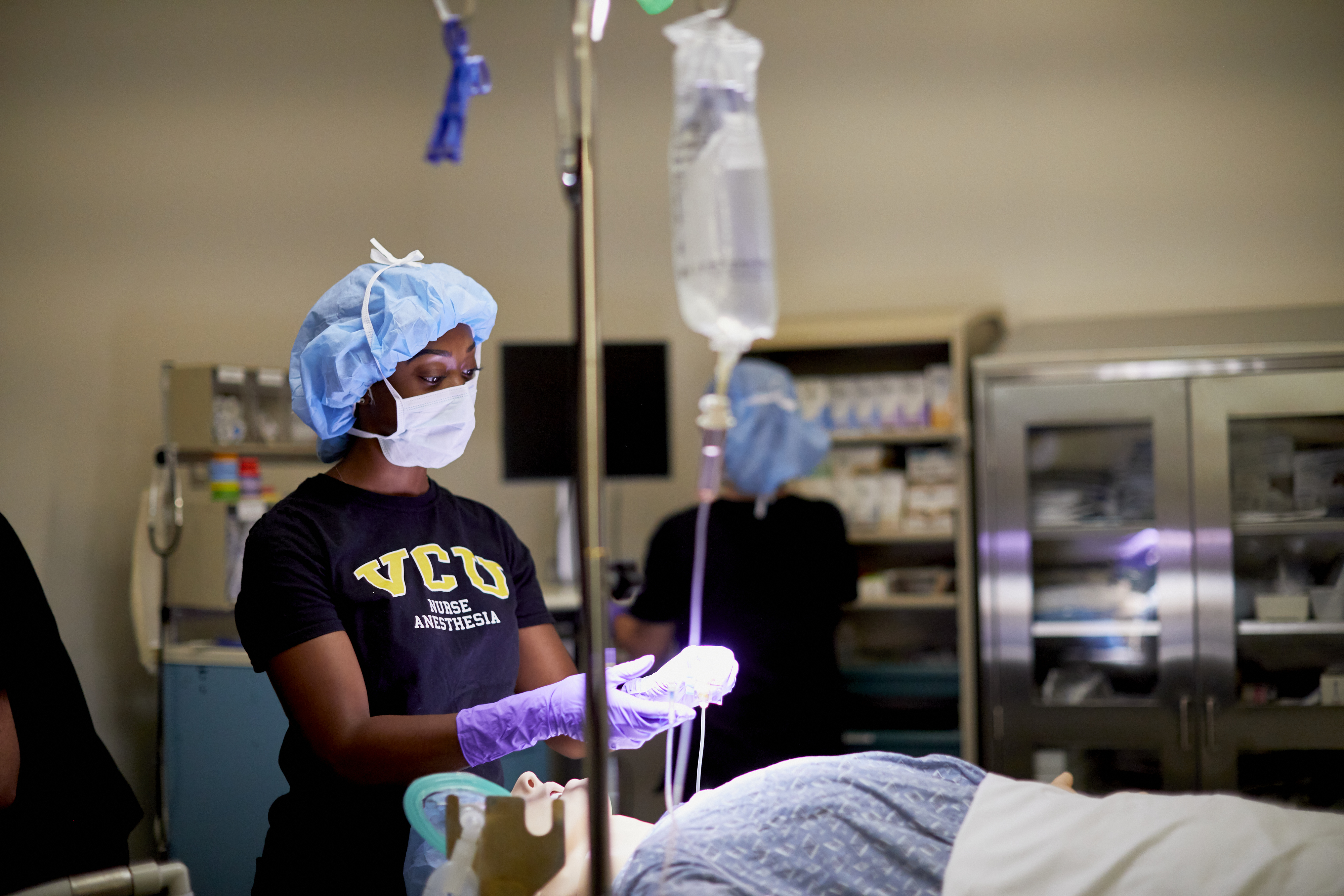 Black female nurse wearing VCU Nurse Anesthesia shirt practicing anesthesia techniques on simulation mannequin.